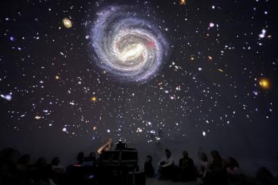 Dôme gonflable noir avec motif de galaxie, utilisé pour des projections, installé dans un gymnase.