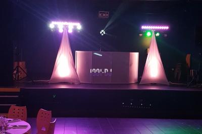 Un DJ mixe sur une scène éclairée par des lumières colorées dans une salle sombre avec un écran projeté.