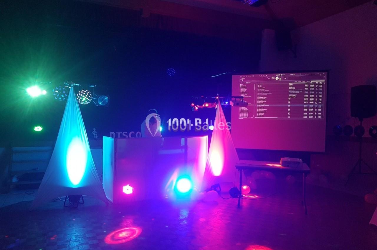 Un DJ mixe sur une scène éclairée par des lumières colorées, avec un écran projetant une playlist en arrière-plan.