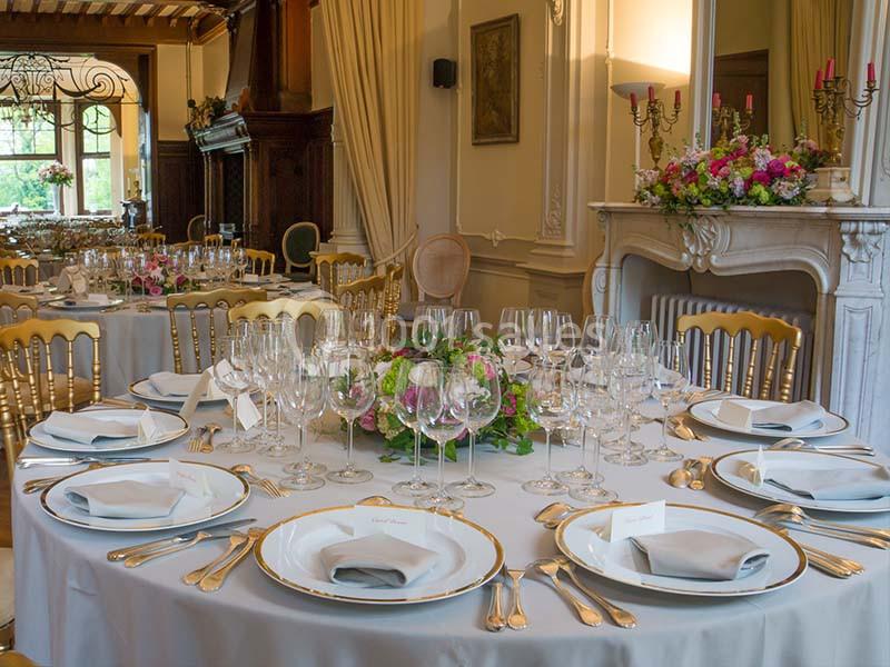 Tables élégamment dressées avec nappes blanches, vaisselle raffinée, verres et centres de table fleuris dans une salle chic.