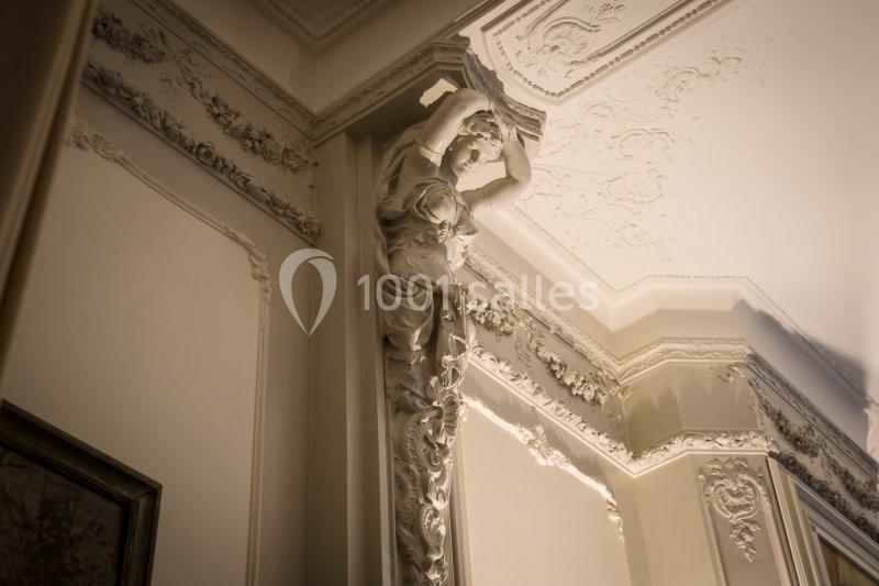 Sculpture décorative en forme de femme soutenant un plafond orné de moulures dans un intérieur classique.