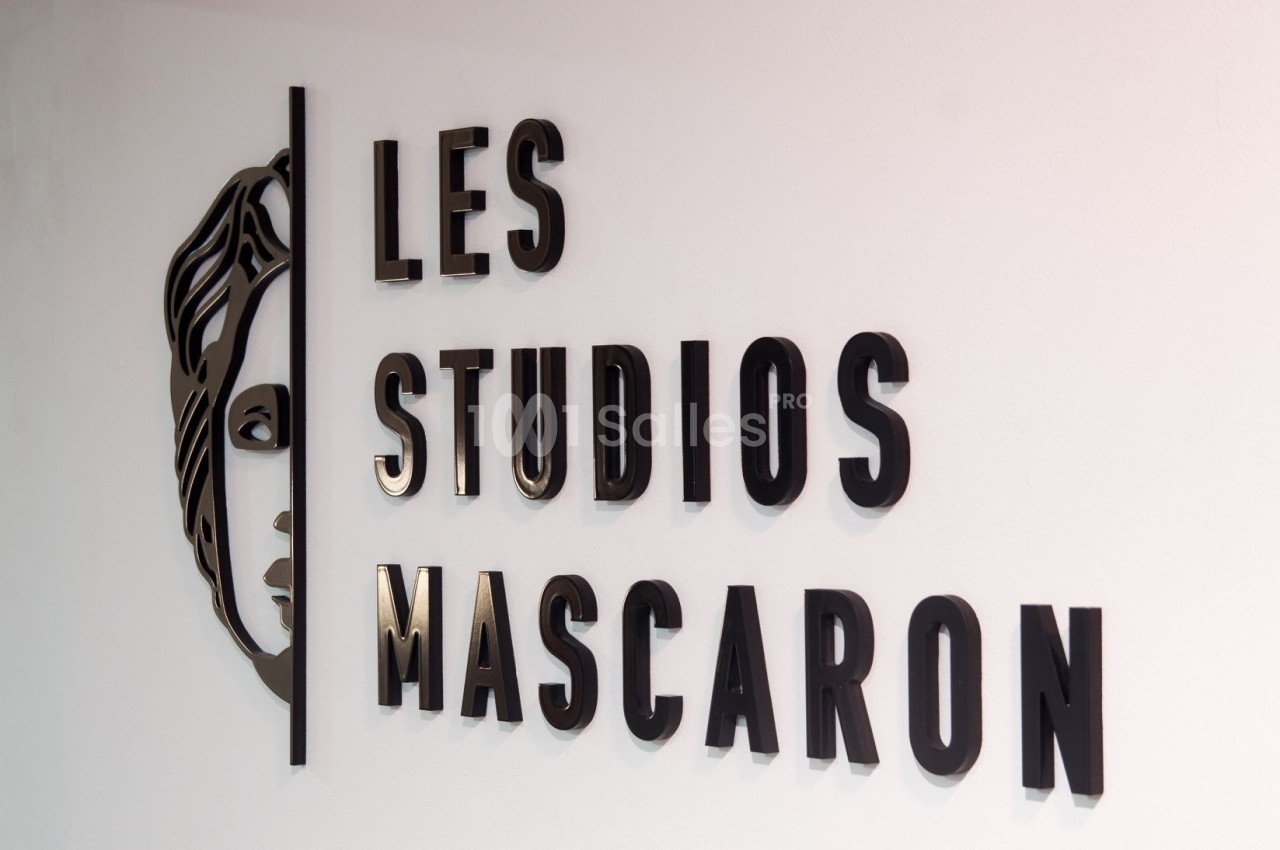 Logo mural des ’Studios Mascaron’ avec un visage stylisé à gauche, en lettres noires sur fond blanc.