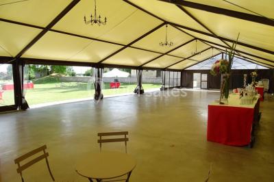 Bâtiment en pierre avec toit en pente, tables et chaises disposées sur une terrasse et une pelouse au premier plan.