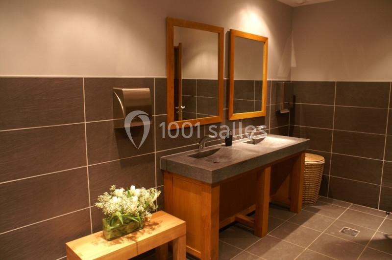 Salle de bain moderne avec deux lavabos, miroirs en bois, carrelage gris et banc en bois décoré de fleurs.