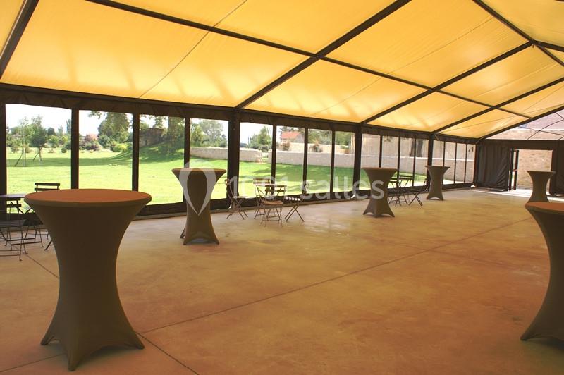 Intérieur d'une tente événementielle avec tables hautes et chaises, donnant sur un espace extérieur verdoyant.