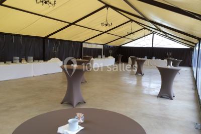 Bâtiment en pierre avec toit en pente, tables et chaises disposées sur une terrasse et une pelouse au premier plan.