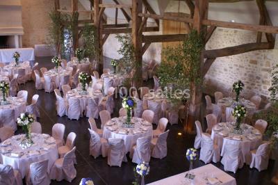 Bâtiment en pierre avec toit en pente, tables et chaises disposées sur une terrasse et une pelouse au premier plan.