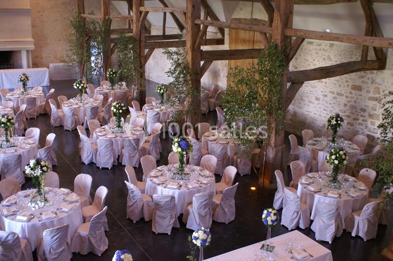 Salle de réception avec tables rondes décorées de nappes blanches, chaises houssées et arrangements floraux élégants.