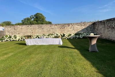 Bâtiment en pierre avec toit en pente, tables et chaises disposées sur une terrasse et une pelouse au premier plan.
