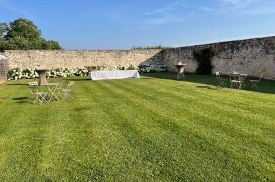 Bâtiment en pierre avec toit en pente, tables et chaises disposées sur une terrasse et une pelouse au premier plan.
