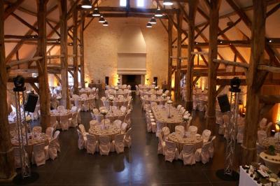 Bâtiment en pierre avec toit en pente, tables et chaises disposées sur une terrasse et une pelouse au premier plan.