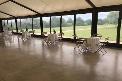 Bâtiment en pierre avec toit en pente, tables et chaises disposées sur une terrasse et une pelouse au premier plan.