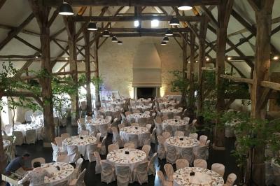 Bâtiment en pierre avec toit en pente, tables et chaises disposées sur une terrasse et une pelouse au premier plan.