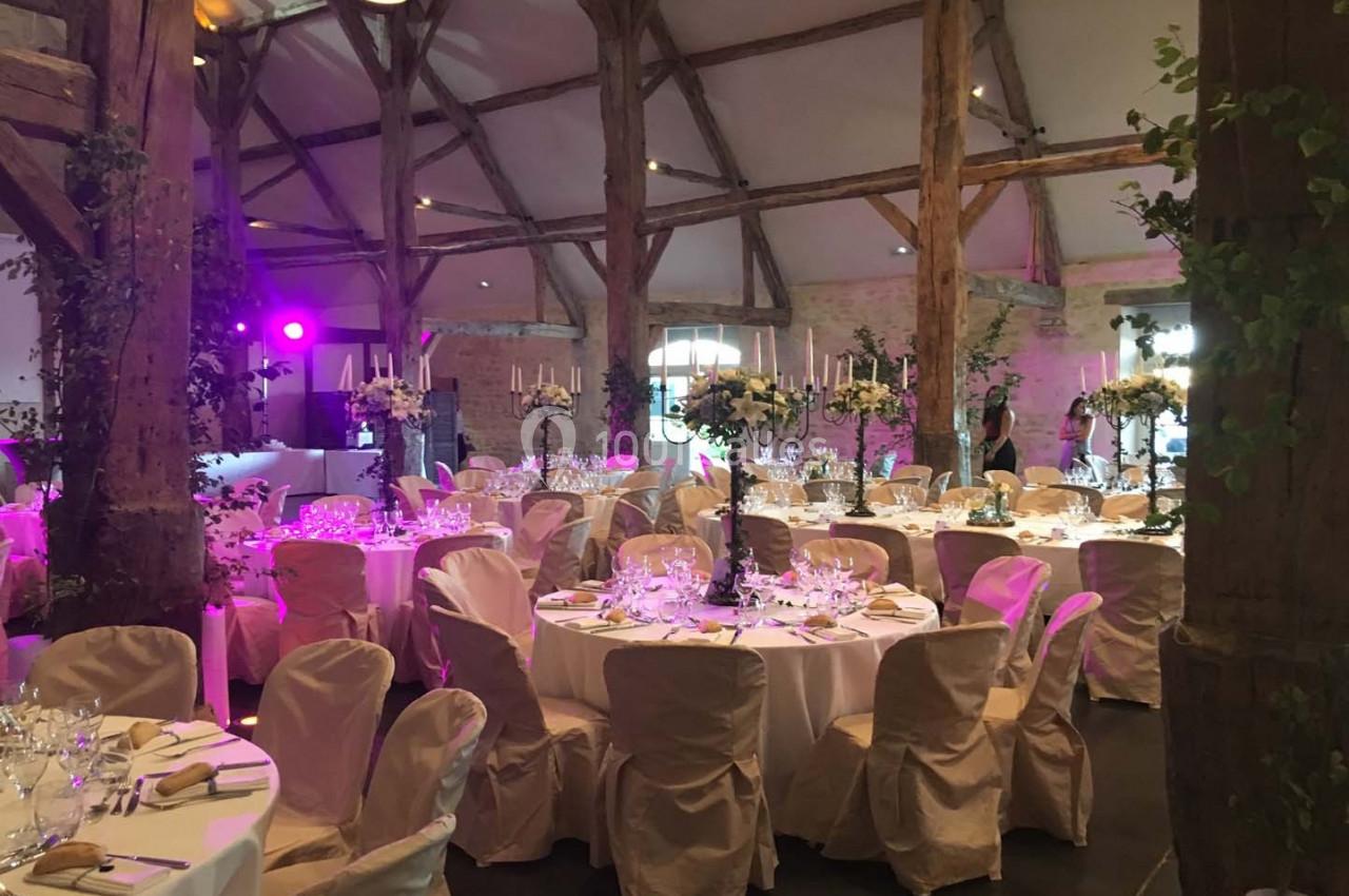 Salle de réception décorée avec des tables rondes, nappes blanches, chandeliers et éclairage tamisé.