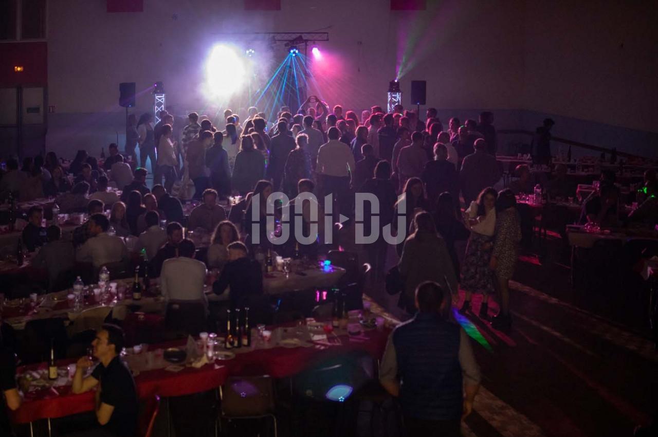 Salle remplie de convives assis et debout, éclairée par des lumières colorées et une ambiance festive.