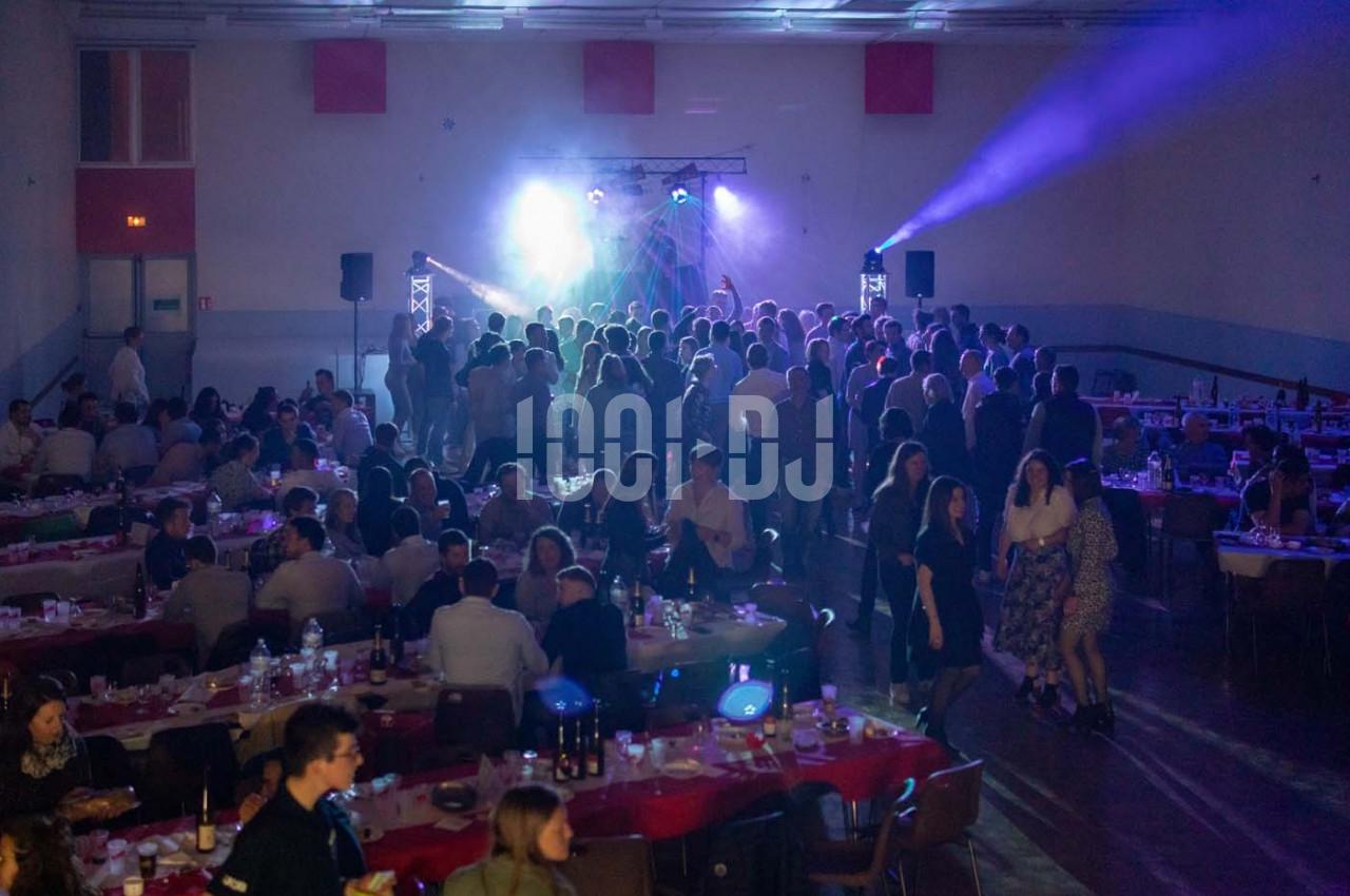 Salle de réception avec des tables dressées et des invités dansant sous des jeux de lumière sur une scène.