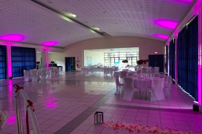 Grande salle en bois avec charpente apparente, éclairages rouges, matériel de sonorisation et espace vide au centre.