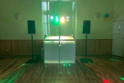 Salle de réception avec piste en parquet, éclairage coloré et équipement audio installé devant un rideau.