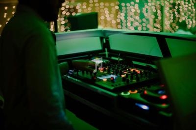 Un DJ manipule une table de mixage éclairée dans une ambiance tamisée avec des lumières floues en arrière-plan.