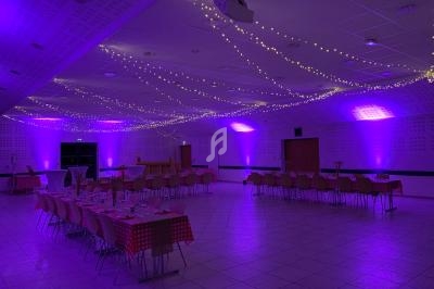 Salle de réception décorée avec des guirlandes lumineuses et des tables dressées sous un éclairage violet.