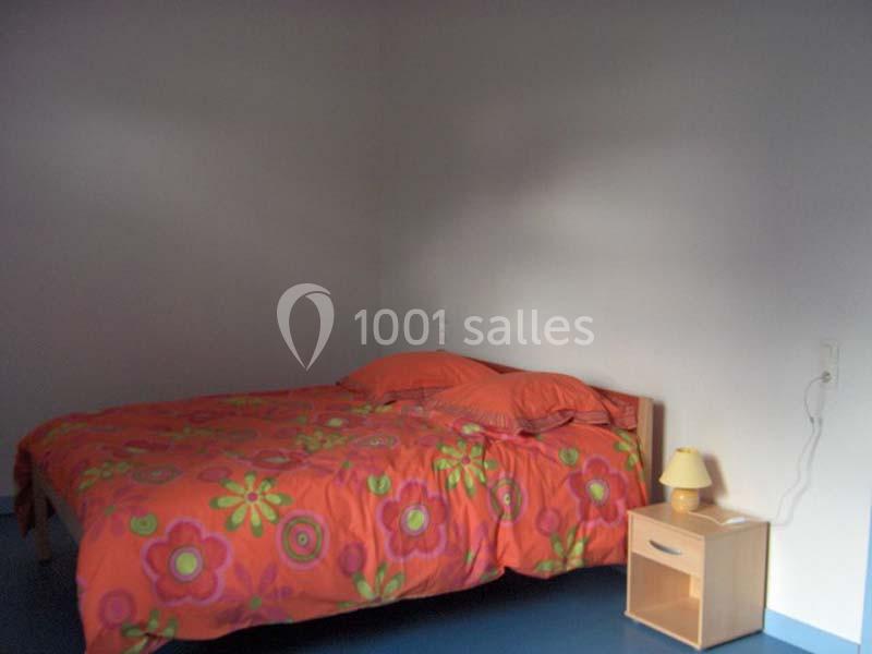 Lit double avec une housse colorée à motifs floraux, accompagné d'une table de chevet en bois avec une lampe.