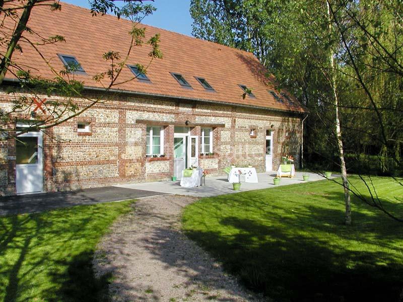 Bâtiment en briques avec toit en tuiles rouges, entouré d'un jardin verdoyant et de quelques arbres.
