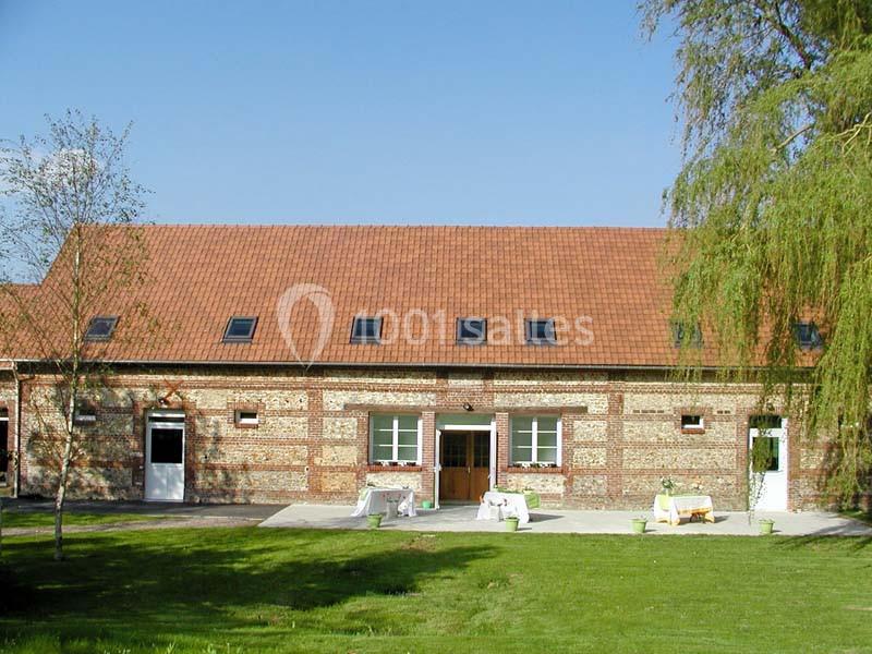 Bâtiment en briques avec toit en tuiles rouges, entouré d'une pelouse et d'arbres sous un ciel dégagé.