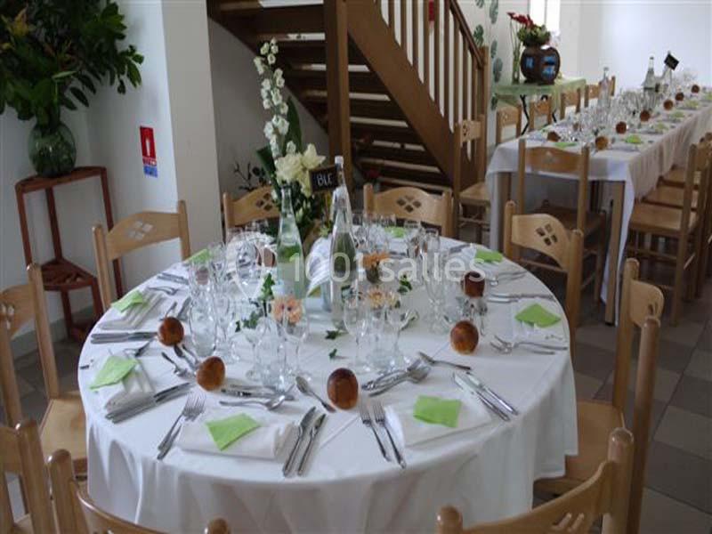 Table ronde dressée pour un repas, avec nappes blanches, serviettes vertes, verres, couverts et décor floral.