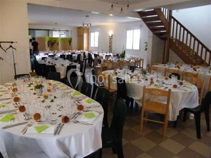 Salle de réception aménagée avec des tables rondes dressées pour un repas, décorées de serviettes vertes et de pains…