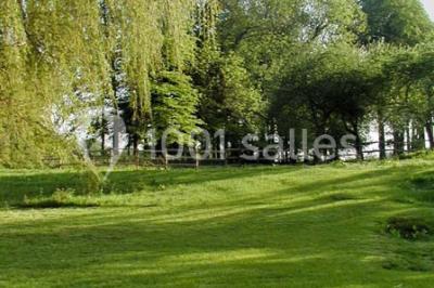 Un jardin verdoyant avec des arbres, de l'herbe fraîchement tondue, un banc en pierre et une clôture en arrière-plan.