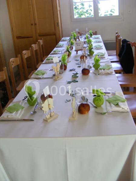 Table dressée pour un repas, décorée avec des pommes, des serviettes vertes et des petits objets en bois.