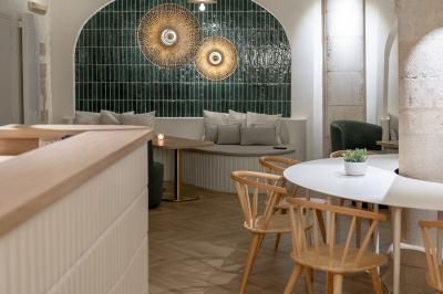 Salle lumineuse avec grandes fenêtres ouvertes sur une rue pavée, mobilier moderne et murs en pierre apparente.