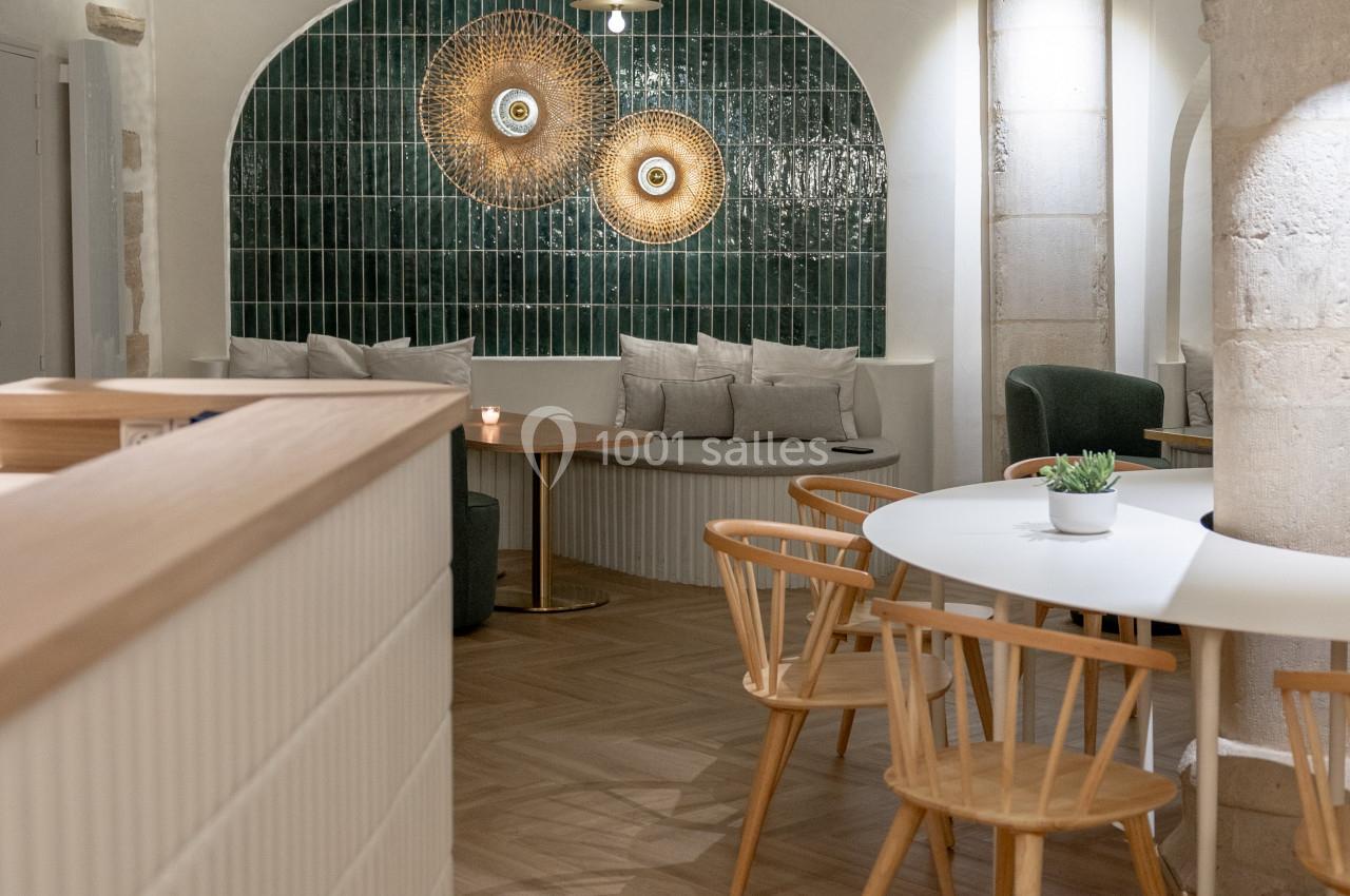 Intérieur d'un café moderne avec tables en bois, chaises design et mur décoré de carreaux verts et d'art mural.