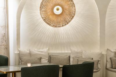 Salle lumineuse avec grandes fenêtres ouvertes sur une rue pavée, mobilier moderne et murs en pierre apparente.