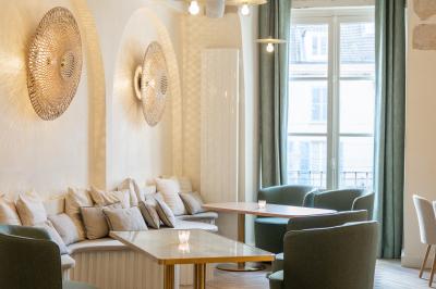 Salle lumineuse avec grandes fenêtres ouvertes sur une rue pavée, mobilier moderne et murs en pierre apparente.