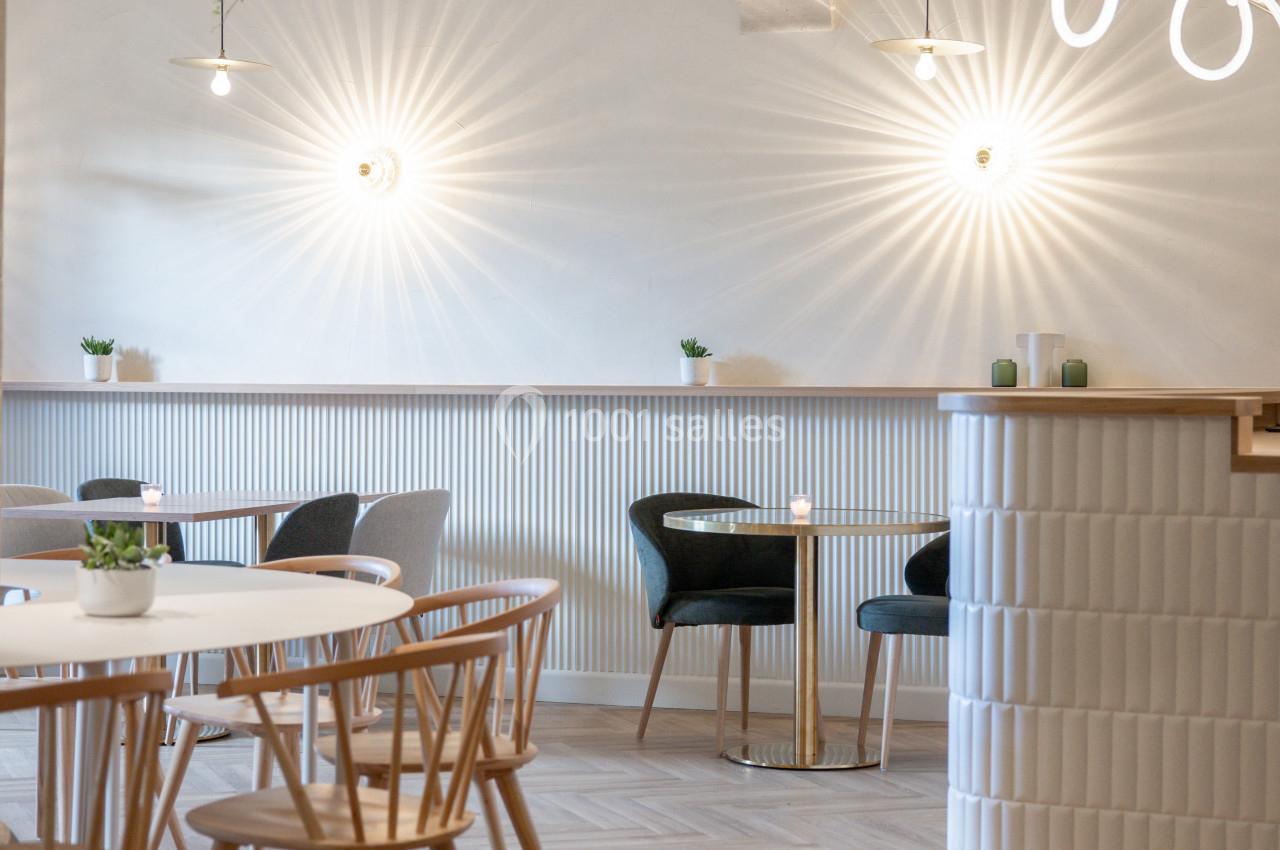 Salle lumineuse avec mobilier en bois clair, chaises modernes, plantes décoratives et éclairage suspendu.