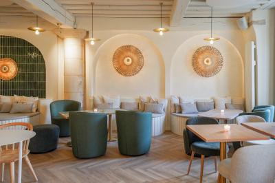 Salle lumineuse avec grandes fenêtres ouvertes sur une rue pavée, mobilier moderne et murs en pierre apparente.