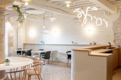 Salle lumineuse avec grandes fenêtres ouvertes sur une rue pavée, mobilier moderne et murs en pierre apparente.