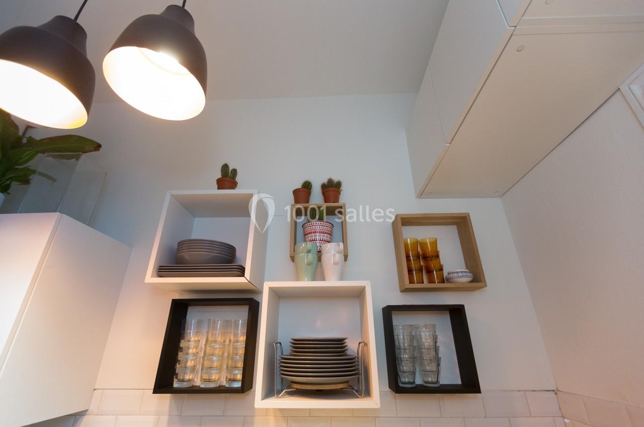 Étagères murales avec vaisselle, verres et plantes en pot dans une cuisine lumineuse au design moderne.