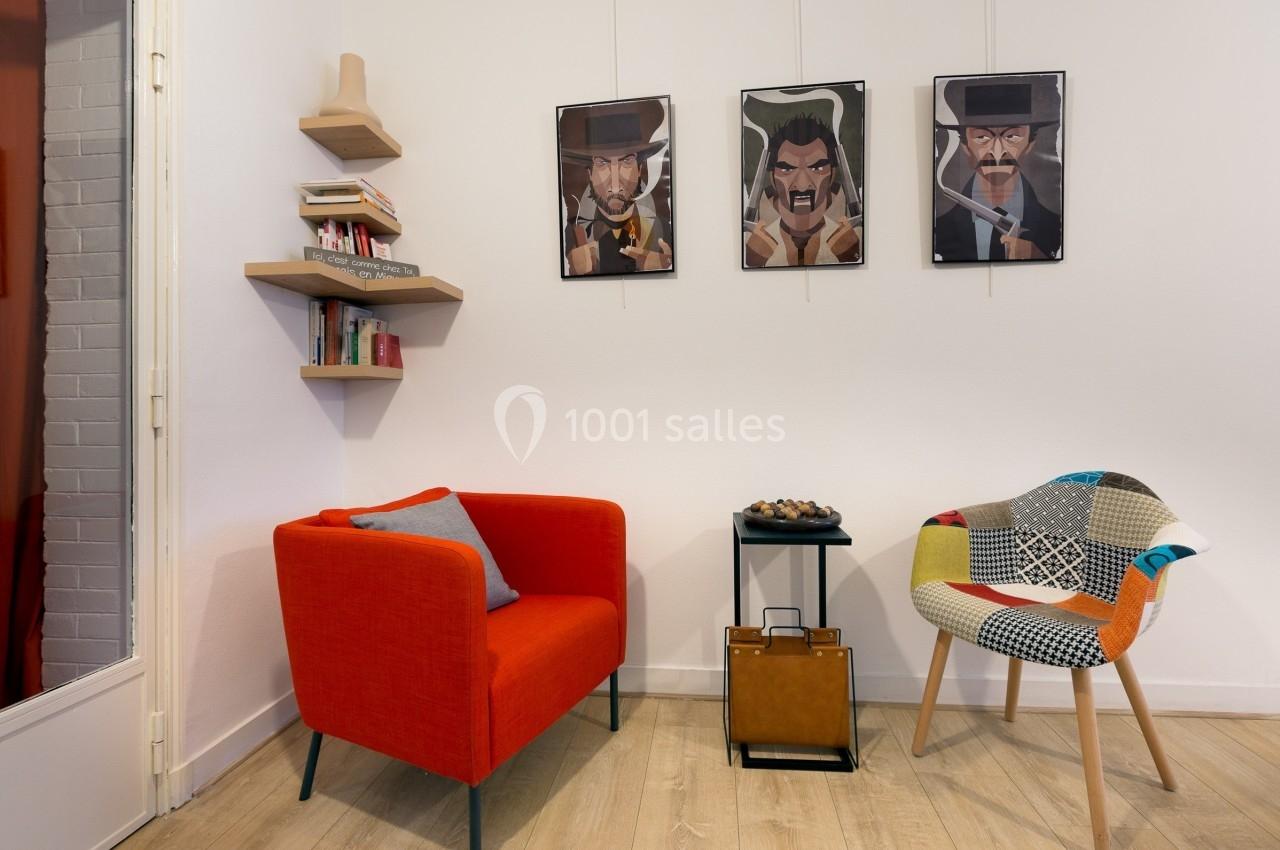 Deux fauteuils colorés, une table basse et des étagères murales dans un salon décoré de portraits encadrés.