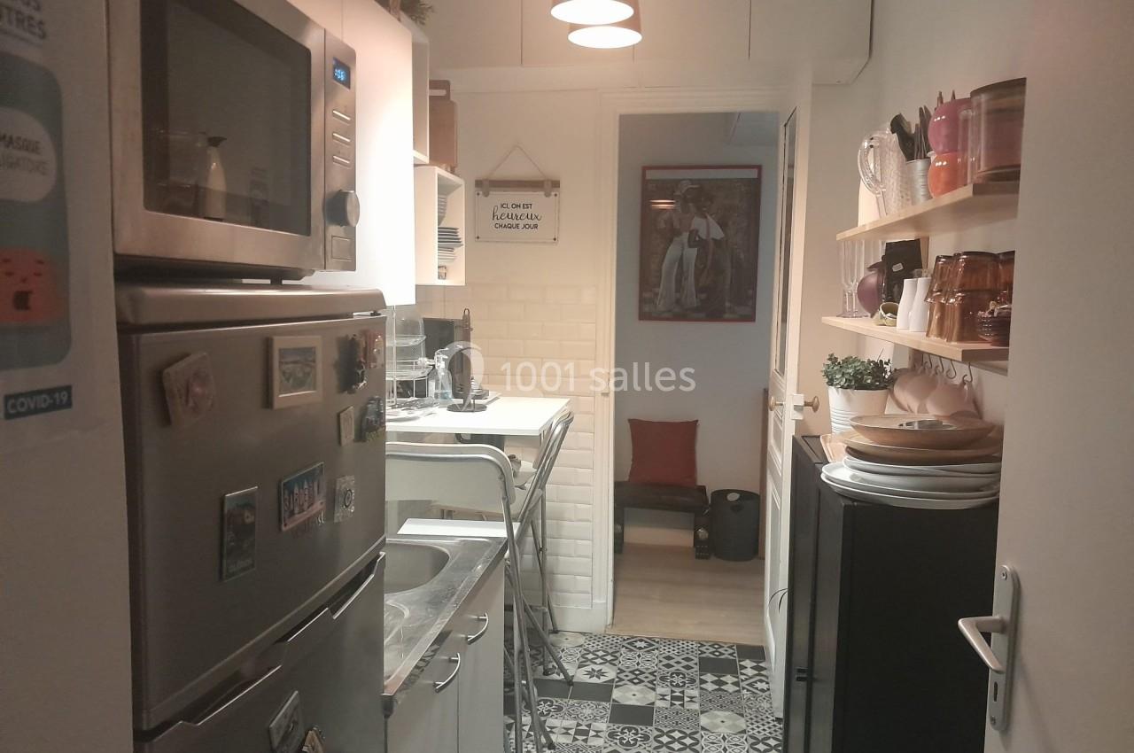 Cuisine étroite avec électroménagers, étagères murales, carrelage au sol et lumière suspendue.