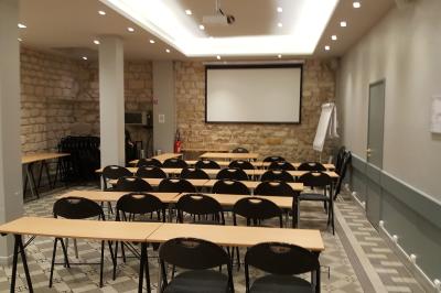 Salle de classe vide avec des tables blanches, des chaises bleues et un tableau de conférence au fond.