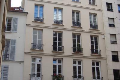 Salle de classe vide avec des tables blanches, des chaises bleues et un tableau de conférence au fond.