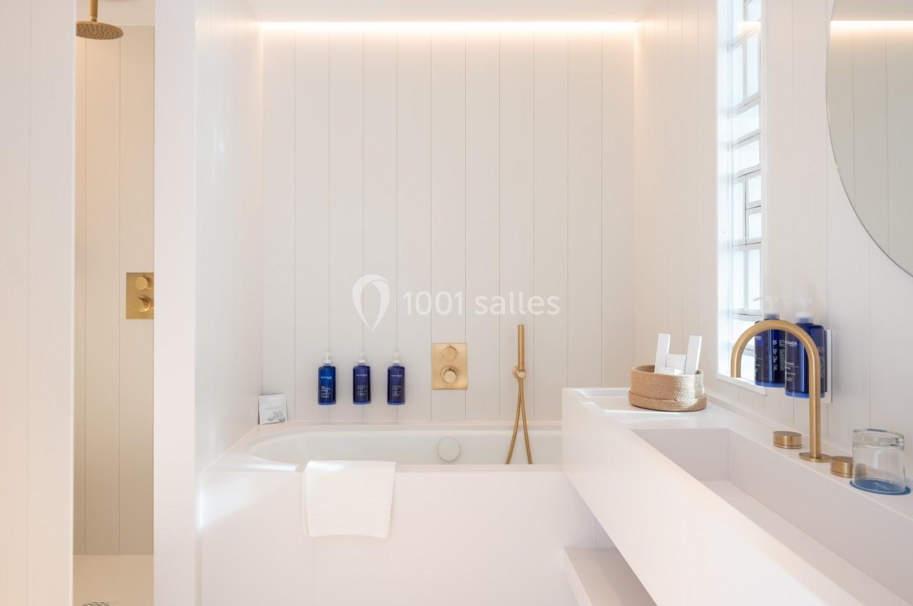 Salle de bain lumineuse avec baignoire, robinetterie dorée, douche à l'italienne et étagères blanches.