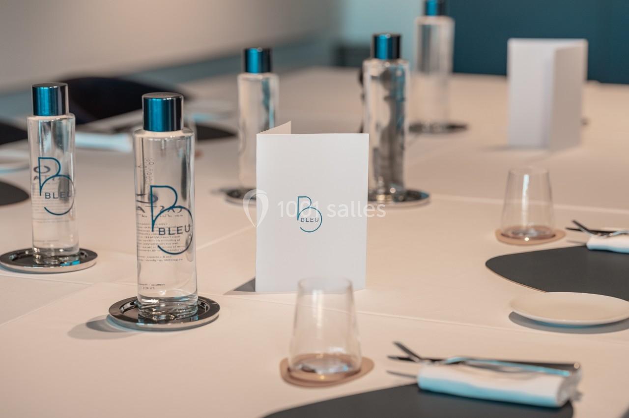 Table dressée avec des bouteilles d'eau, des verres, des couverts et un menu, dans une salle lumineuse et moderne.