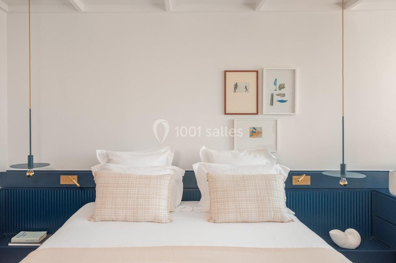 Lit double avec coussins beiges, tables de chevet intégrées, suspensions modernes et décorations murales minimalistes.