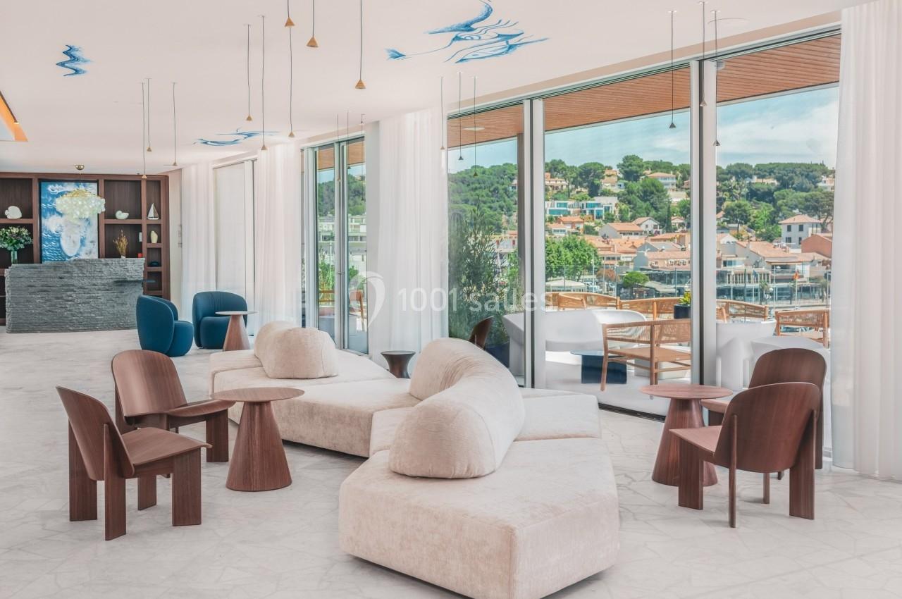 Salon lumineux avec mobilier moderne, grandes baies vitrées donnant sur une terrasse et vue sur un paysage urbain verdoyant.