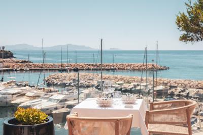 Table dressée pour deux avec vue sur un port de plaisance, des voiliers et la mer sous un ciel dégagé.
