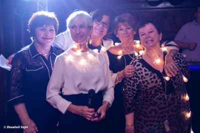 Un couple danse ensemble dans une salle décorée de ballons, entouré de quelques invités en arrière-plan.