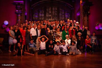 Un couple danse ensemble dans une salle décorée de ballons, entouré de quelques invités en arrière-plan.